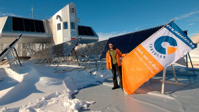 Technicien tenant un drapeau Consolar devant des panneaux solaires installés dans la neige, près d'une station